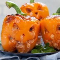 Three orange Halloween Stuffed Peppers carved to look like jack-o-lanterns on a green plate.