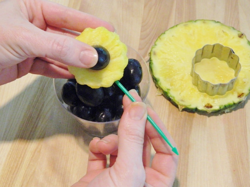 Cut a black grape in half & press on the pineapple flower. Then poke your green pick in the bottom