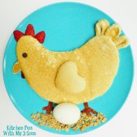 Pancake shaped like a chicken sitting on a boiled egg breakfast on a blue plate