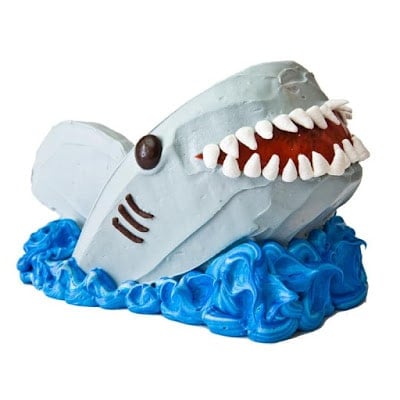 A blue-frosted cake with wave patterns and a large shark decoration made of cake on top