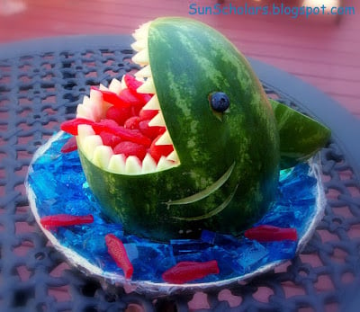 A watermelon carved to resemble a shark's head with Sweedish Fish in its mouth