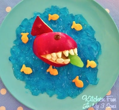 An apple carved and decorated to look like a shark with blue jello resembling water underneath it