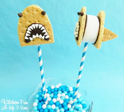 S'mores pops decorated to look like sharks in front of a teal-colored backdrop