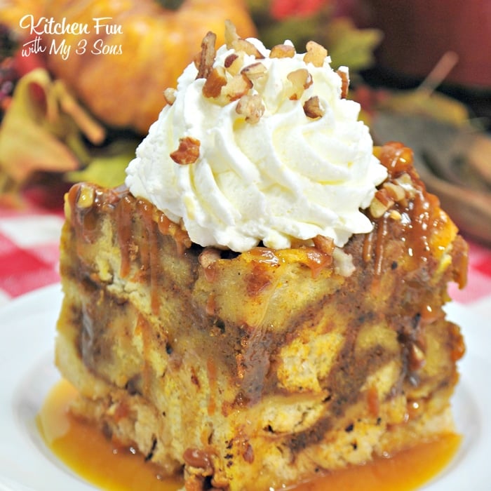 A serving of Slow Cooker Pumpkin Maple French Toast in a pool of maple syrup on a white plate. Gingham and fall decorations form the backdrop.