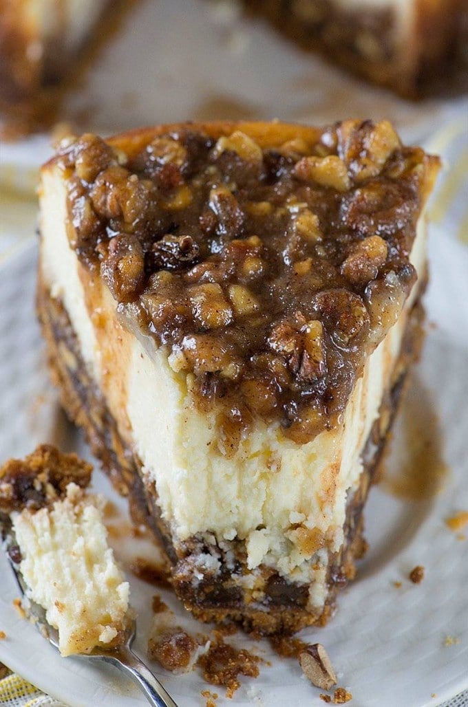 A slice of Pecan Pie Cheesecake on a white plate, with a bite-sized piece cut off and on a fork nearby.