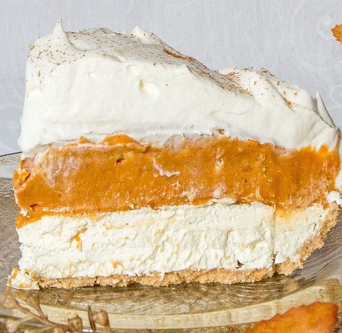 A tall slice of No-Bake Triple Layer Pumpkin Pie on a clear glass plate, with autumn leaf and stem decorations underneath.