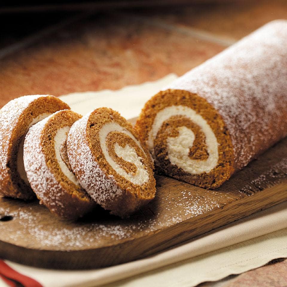 A partially sliced Pumpkin Cake Roll on a cutting board, dusted with powdered sugar.
