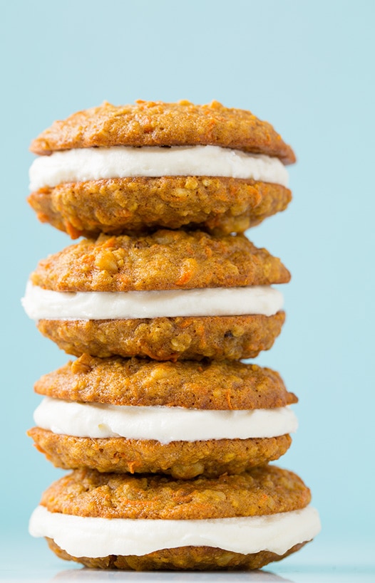Three Carrot Cake Sandwich Cookies in a crooked stack, against a pale blue background.