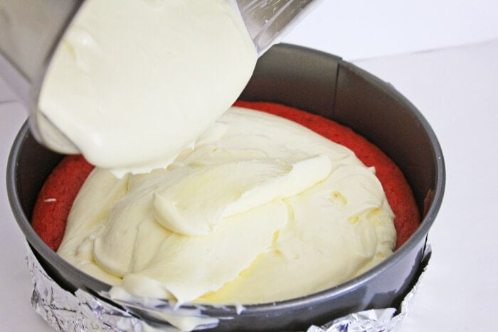 pouring cheesecake over red velvet cake layer