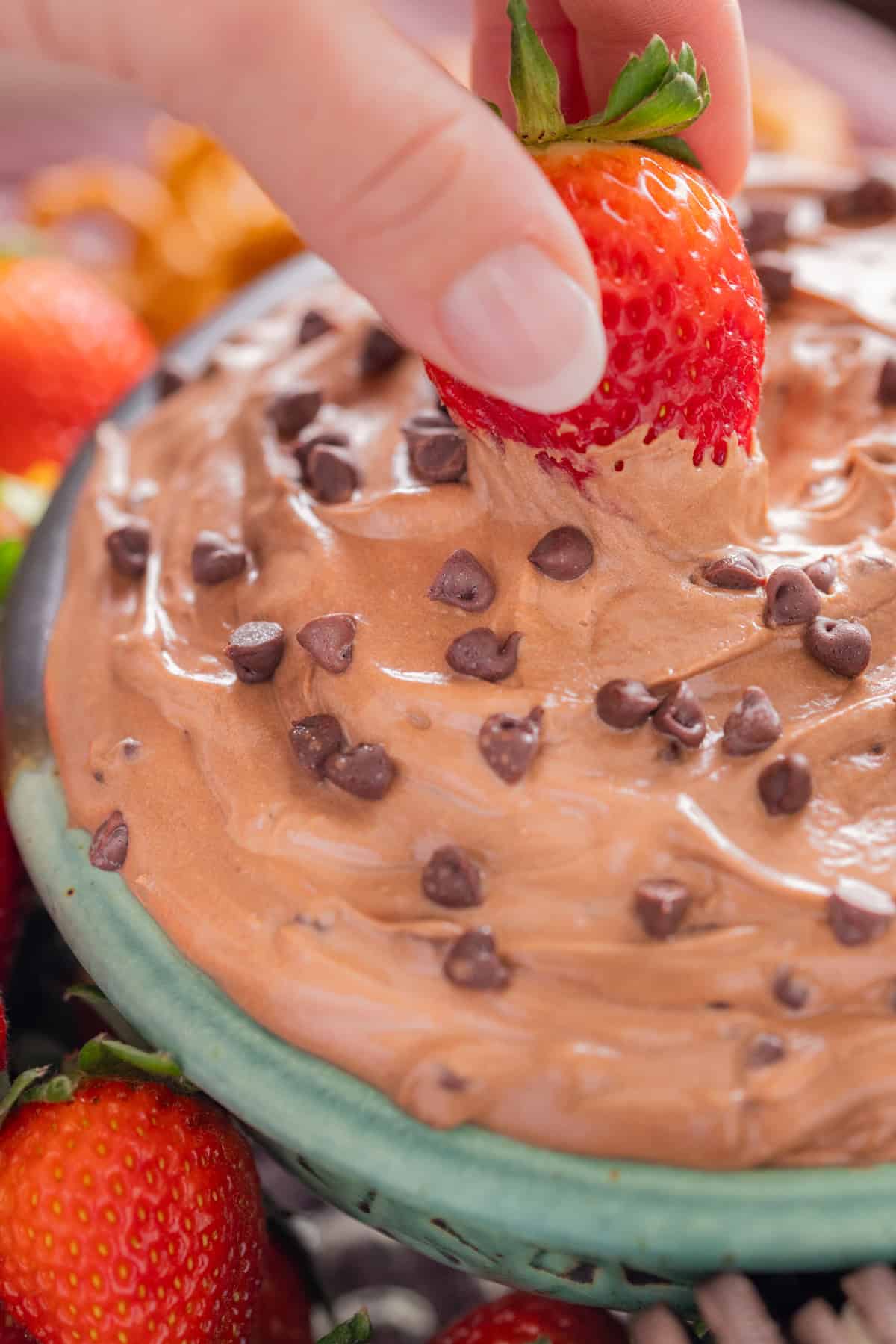 A hand dipping a strawberry into brownie batter dip