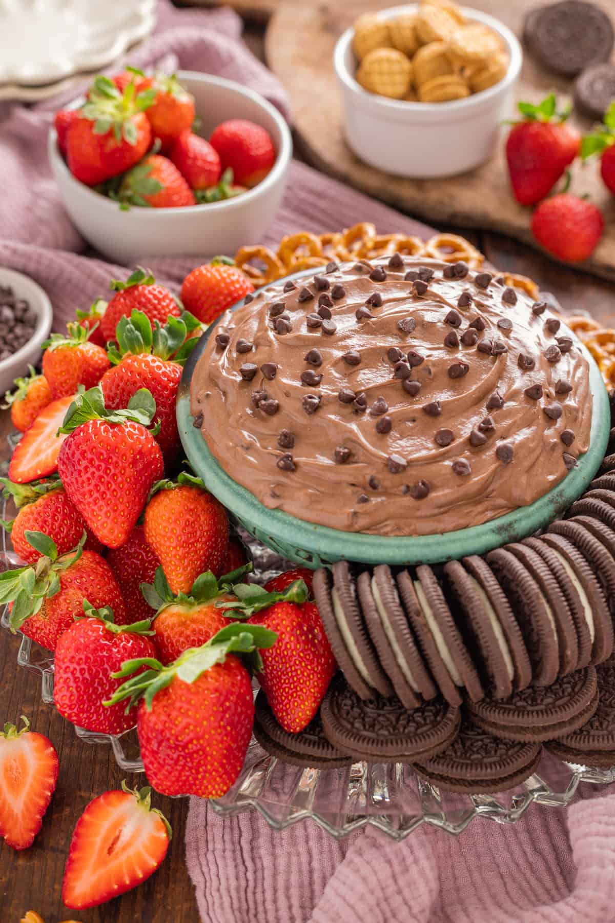 A blue bowl of brownie batter dip surrounded by cookies and strawberries