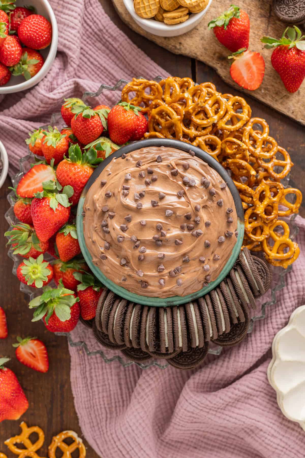 Overhead view of a bowl of brownie batter dip surrounded by cookies, pretzels, and strawberries
