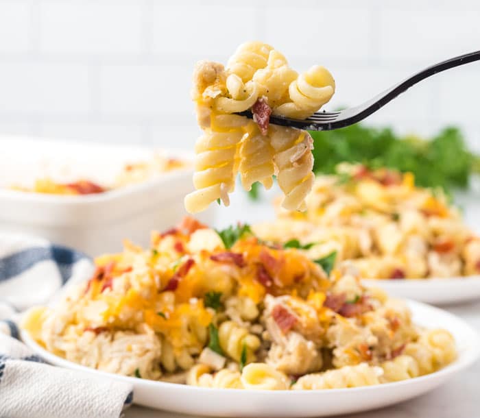 A fork with a few pieces of rotini over a plate of chicken bacon ranch pasta