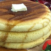 A stack of 3 puffy pancakes topped with butter and syrup