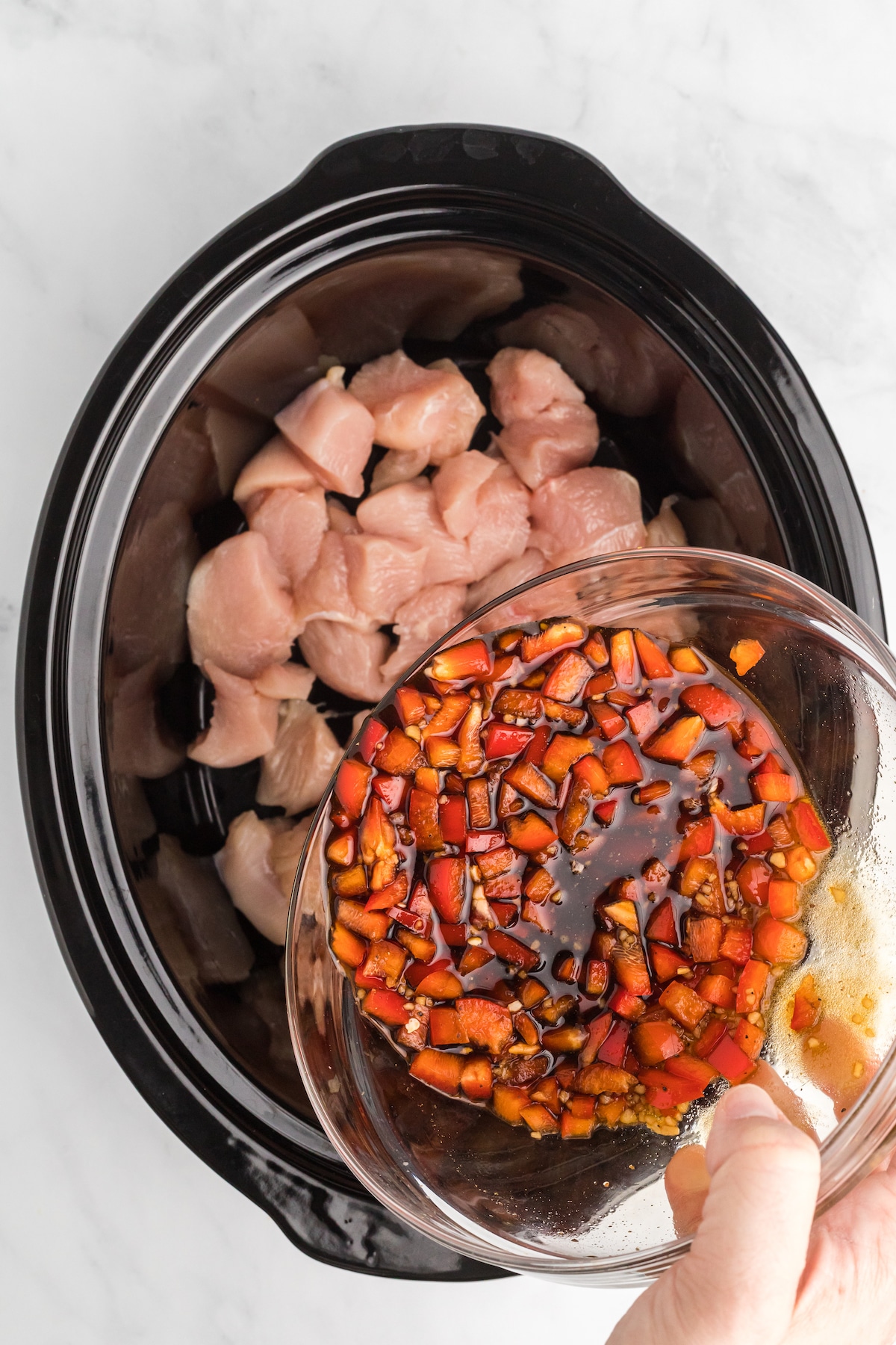 Teriyaki sauce being poured over chunks of chicken breast in a slow cooker