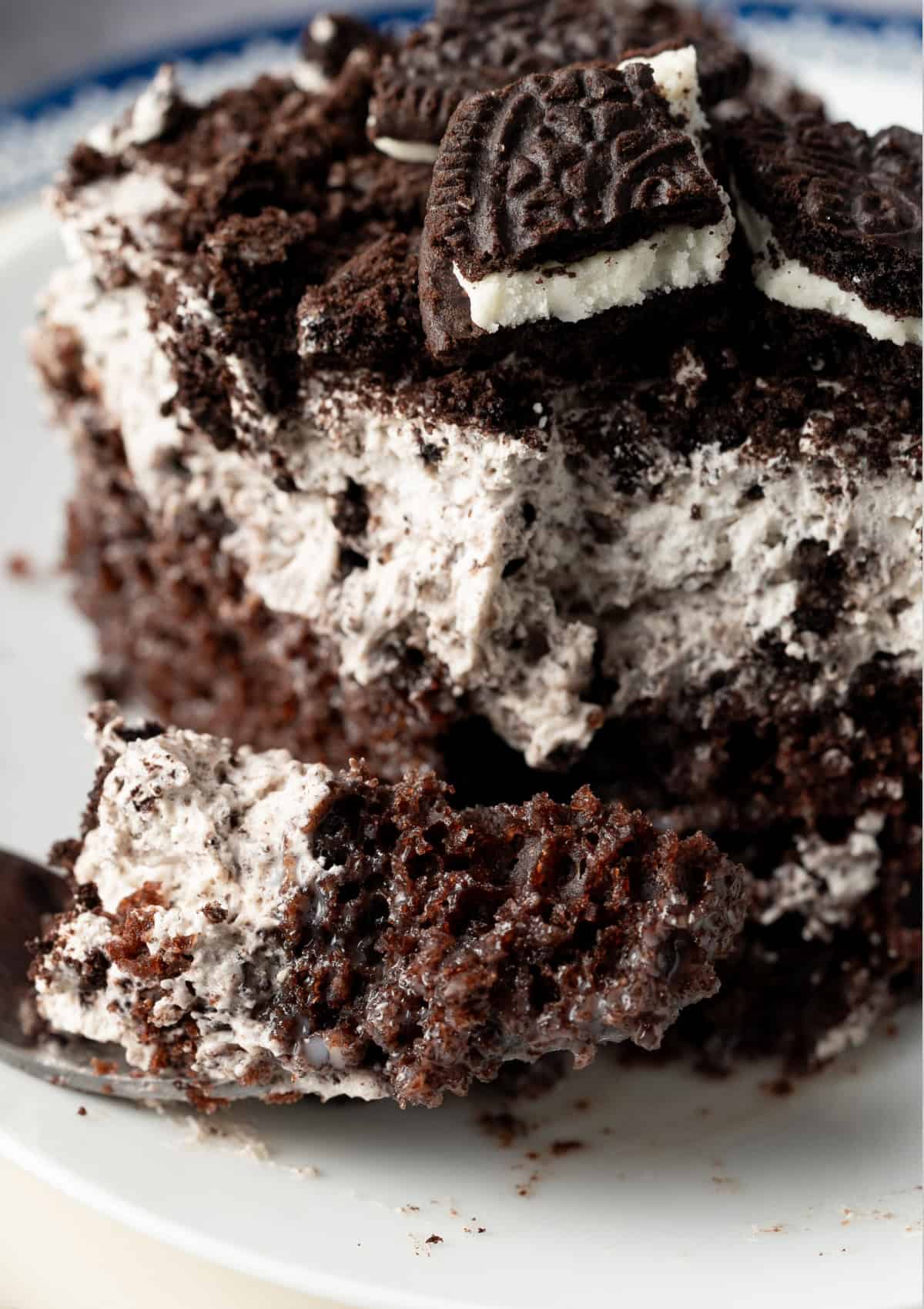 This Oreo Poke Cake is an easy, crowd-pleasing dessert that's loaded with rich chocolate cake, creamy cookies and cream pudding, fluffy whipped topping, and plenty of crushed Oreo cookies. a bite taken from an Oreo poke cake using a fork