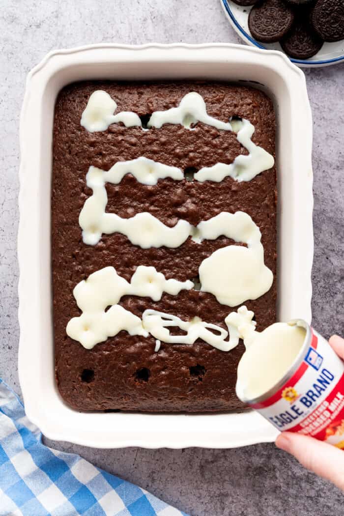 pouring sweetened condensed milk over the chocolate cake