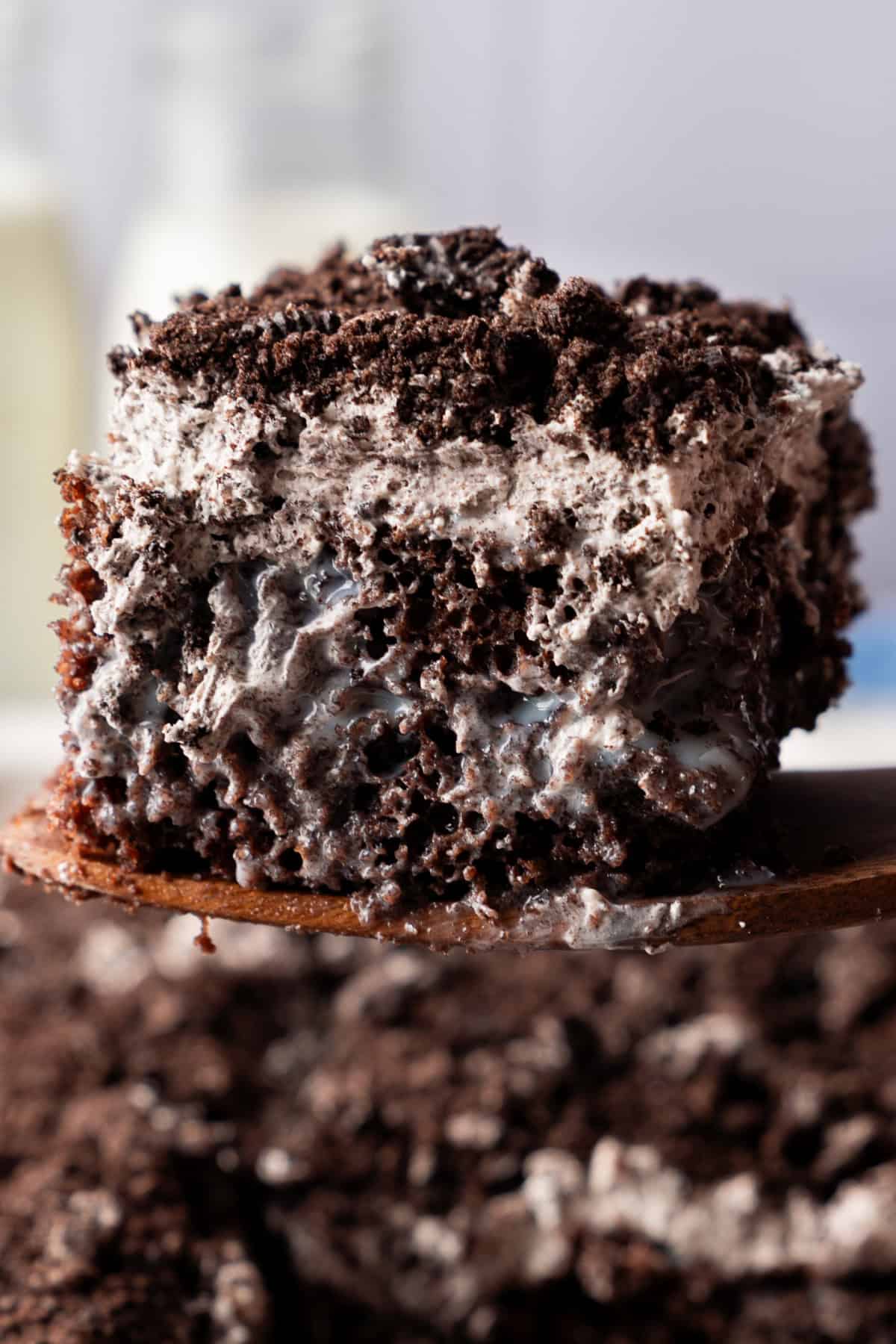 This Oreo Poke Cake is an easy, crowd-pleasing dessert that's loaded with rich chocolate cake, creamy cookies and cream pudding, fluffy whipped topping, and plenty of crushed Oreo cookies. Oreo poke cake slice being lifted out of the pan with a spatula
