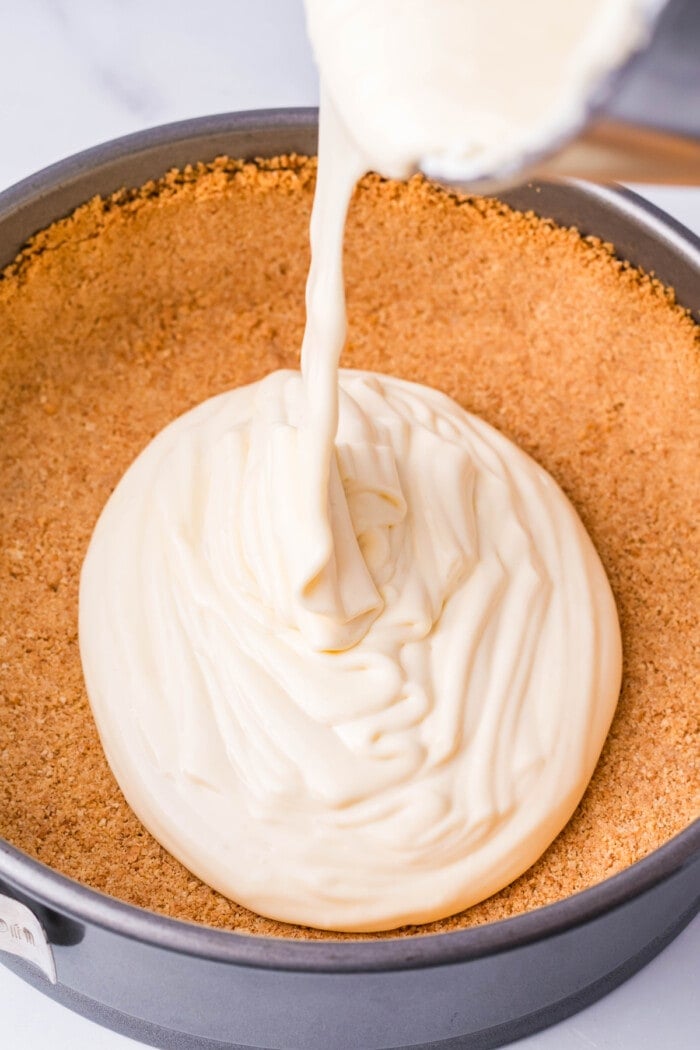 Cheesecake mixture being poured into a graham cracker crust