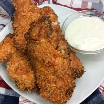 Doritos air fryer chicken tenders on a plate next to white dipping sauce.