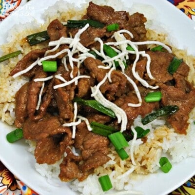 A plate of Instant Pot Mongolian Beef on a bed of rice with scallions and rice noodles sprinkled over the top.