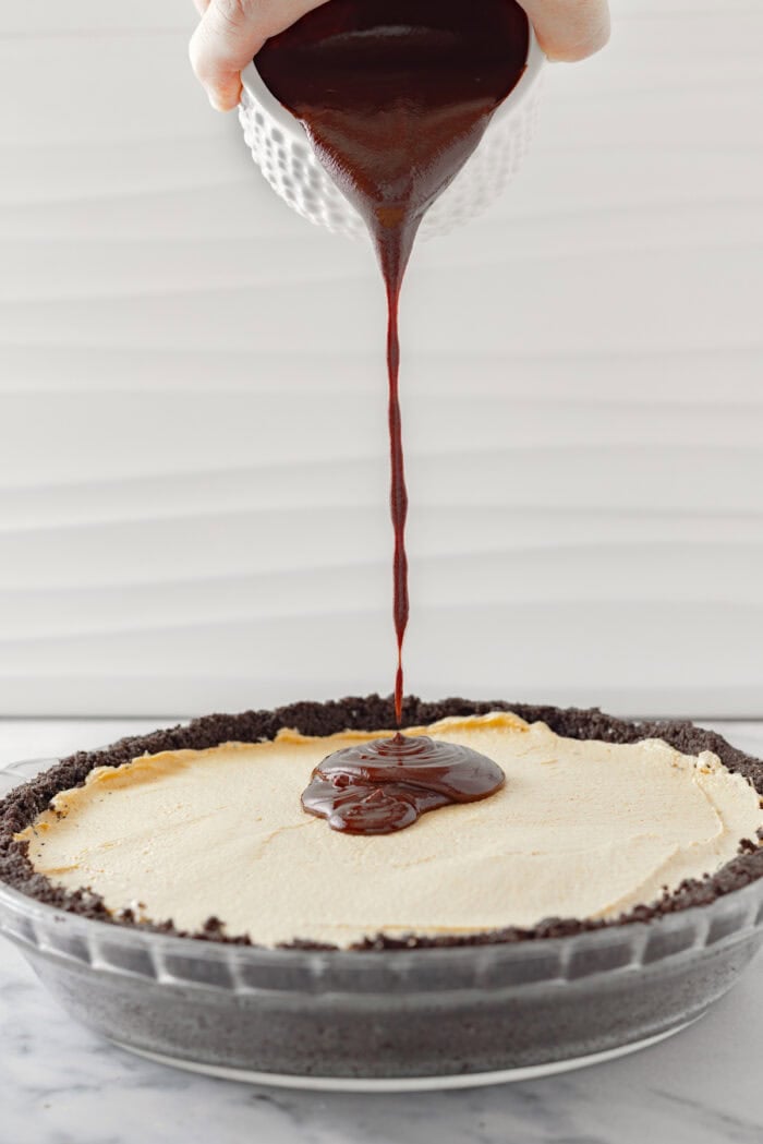 Drizzling chocolate ganache over peanut butter filling in an Oreo crust