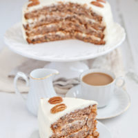 A slice of hummingbird cake on a plate in front of a cup of coffee and the rest of the cake.