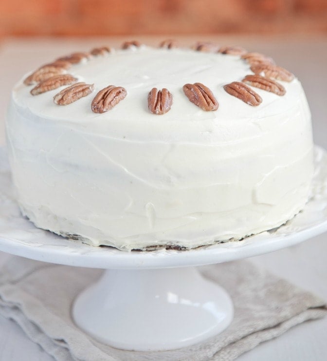 A cake with cream cheese frosting with the edges lined with whole toasted pecans.