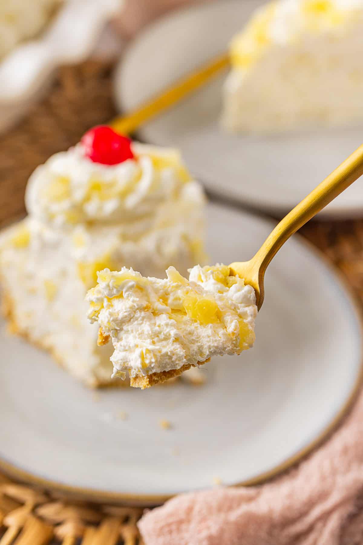 A bite of pineapple pie on a fork in front of a slice on a plate