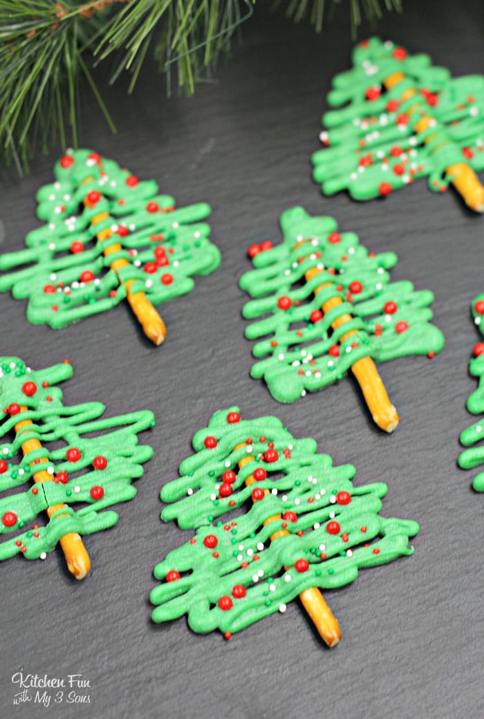 Six chocolate pretzel Christmas tree treats on a black table with pine needles behind them