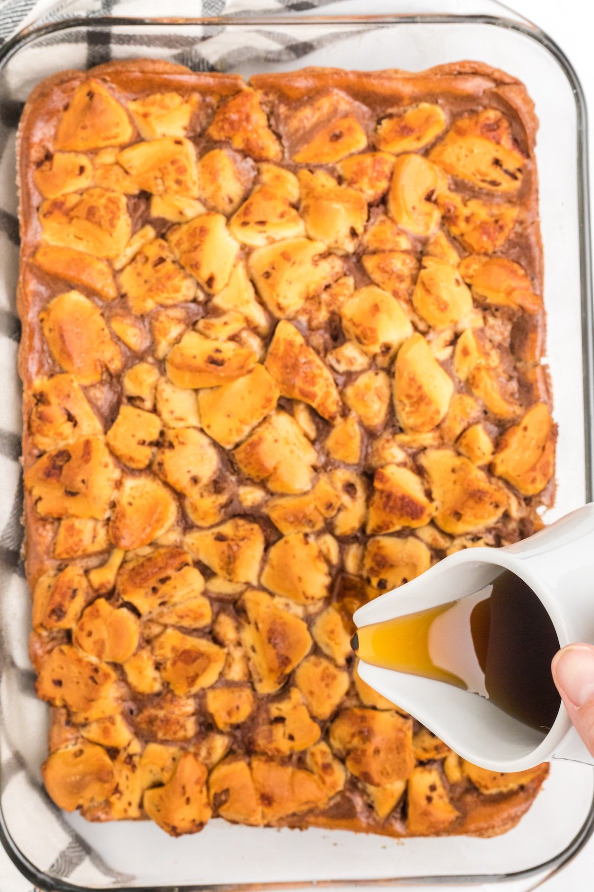 Maple syrup being poured over cinnamon roll casserole