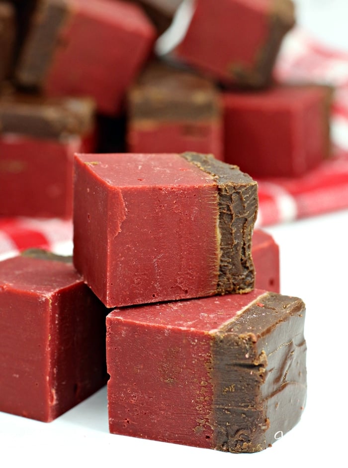 Three squares of red velvet chocolate fudge stacked in the foreground, with more fudge in the background.