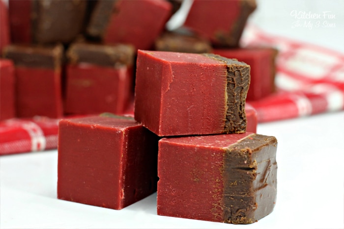 Three squares of red velvet chocolate fudge stacked in the foreground, with more fudge in the background.
