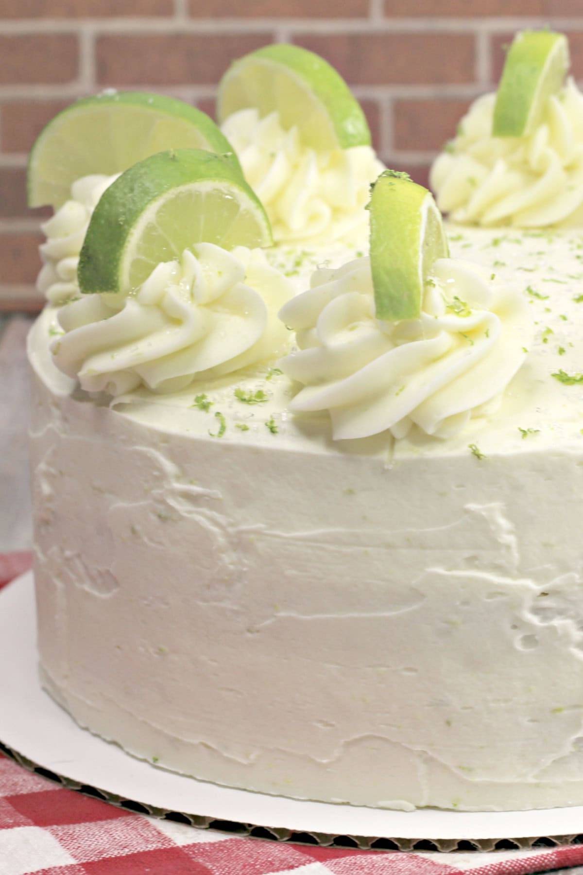 This decadent Margarita Cake features three moist cakes infused with tequila and layered with a tangy, creamy lime frosting. A frosted margarita cake on a cake plate