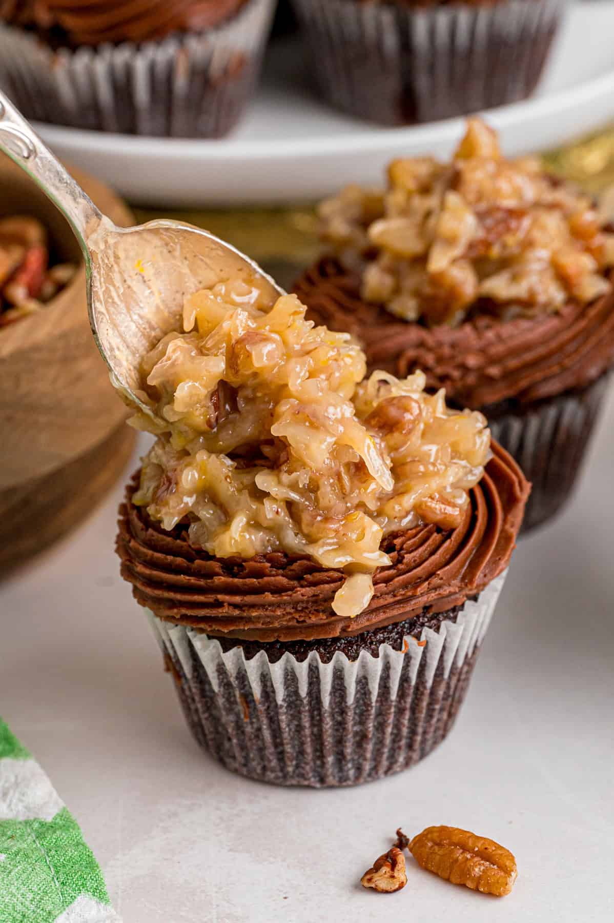 Chocolate cupcakes are filled with a sweet coconut pecan mixture and topped with chocolate buttercream in these German Chocolate Cupcakes. Spooning coconut pecan filling over piped buttercream on a chocolate cupcake