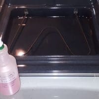 An oven with the door open to reveal a sparkling chamber, next to a bottle of DIY oven cleaner.