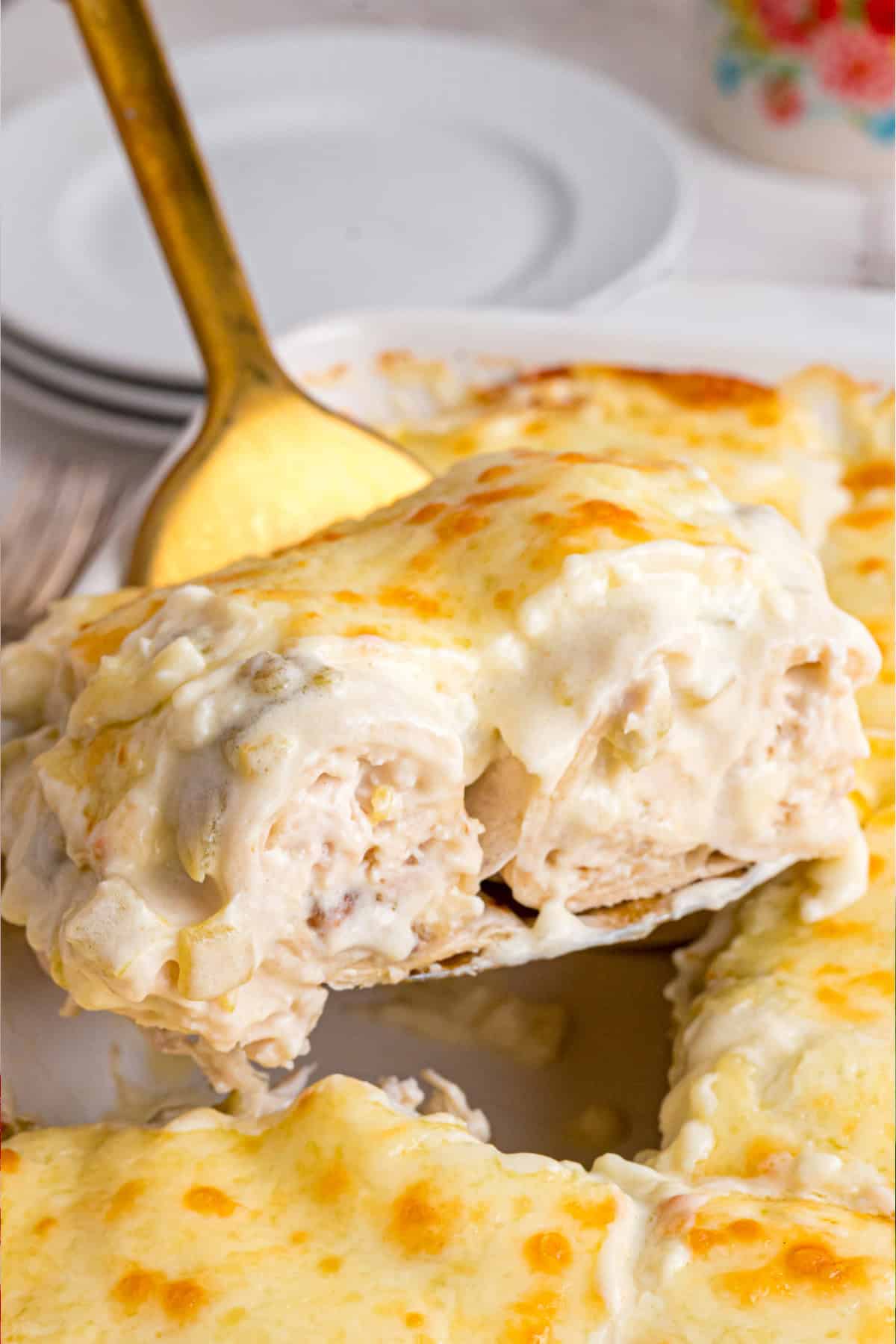 These White Chicken Enchiladas are made with rotisserie chicken, shredded cheese, and a simple sauce made with sour cream and green chiles. lifting a slice of white chicken enchiladas out of a baking dish
