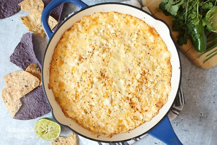 Overhead view of skillet Mexican corn dip in a blue skillet, surrounded by dip ingredients.