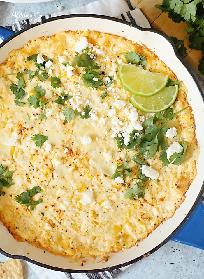 Overhead view of skillet Mexican corn dip in a blue skillet, garnished with cilantro and lime slices.