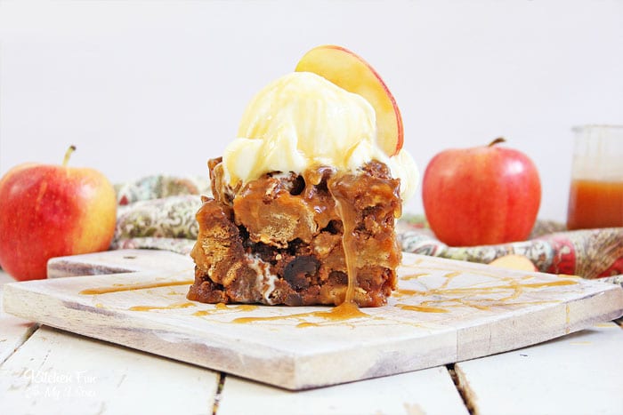 A slice of Slow Cooker Apple Bread Pudding topped with a scoop of ice cream and an apple wedge on a marble cutting board.