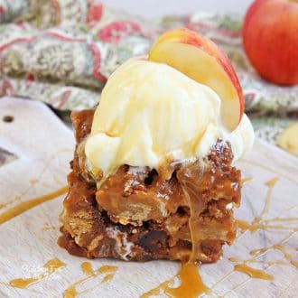 A slice of Slow Cooker Apple Bread Pudding topped with a scoop of ice cream and an apple wedge on a marble cutting board.