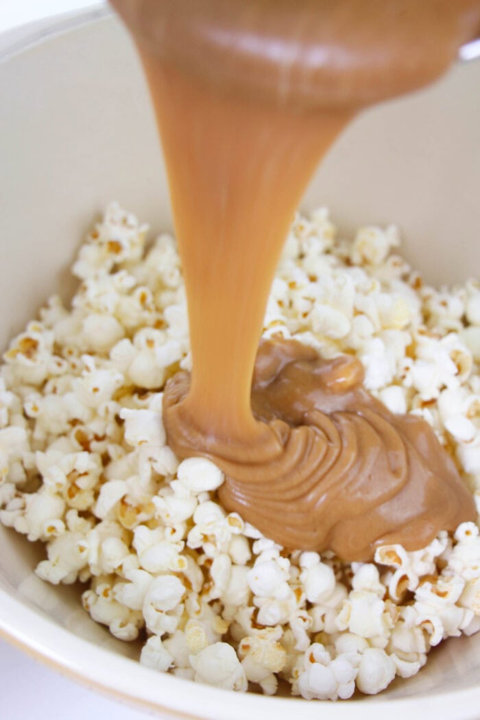This easy Peanut Butter Popcorn recipe uses just 4-ingredients and is the most delicious snack for peanut butter lovers! pouring peanut butter sauce over popcorn