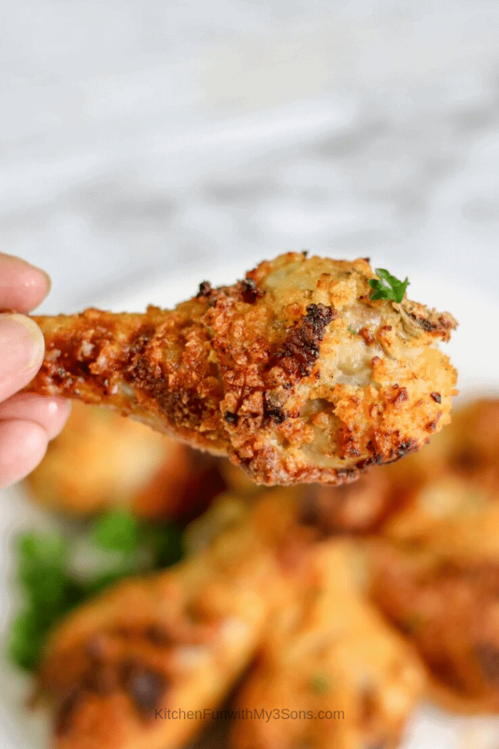 A hand holding a cooked air fryer chicken leg above a plate of prepared legs