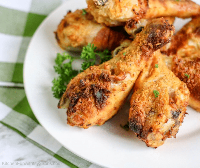 A white plate on a green plaid napkin stacked high with air fryer chicken legs