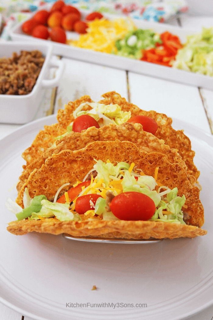 Keto taco shells filled with veggies and meat sitting on a white plate with toppings in background