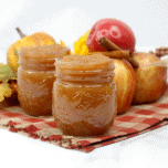 Mason jars filled with homemade applesauce sitting on a plaid napkin with fresh apples and cinnamon sticks