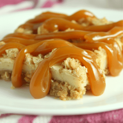 Slice of caramel apple cheesecake bar sitting on a white plate with caramel sauce drizzled over the top