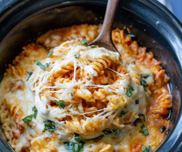 Wooden spoon full of pizza casserole recipe lifting it out of slow cooker