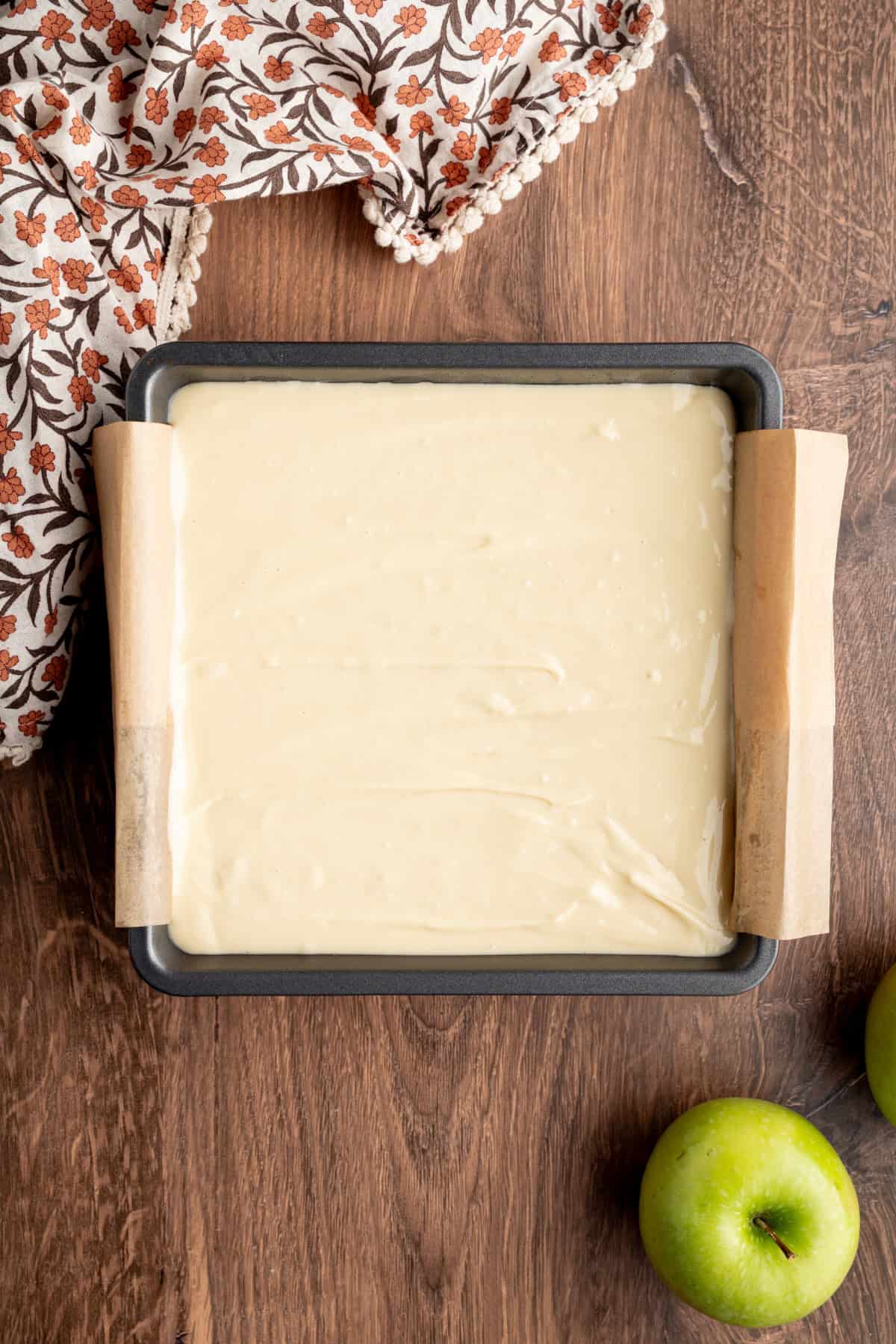 These Caramel Apple Cheesecake Bars combine creamy caramel cheesecake with cinnamon-spiced apples and a buttery oat crumble. cheesecake batter added to a pan ready for baking.