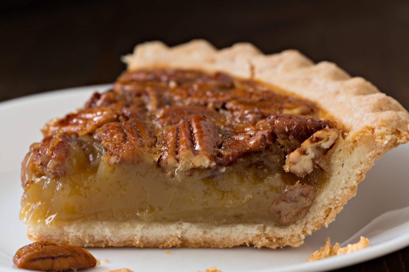 A close up shot of a slice of classic pecan pie on a white saucer. 